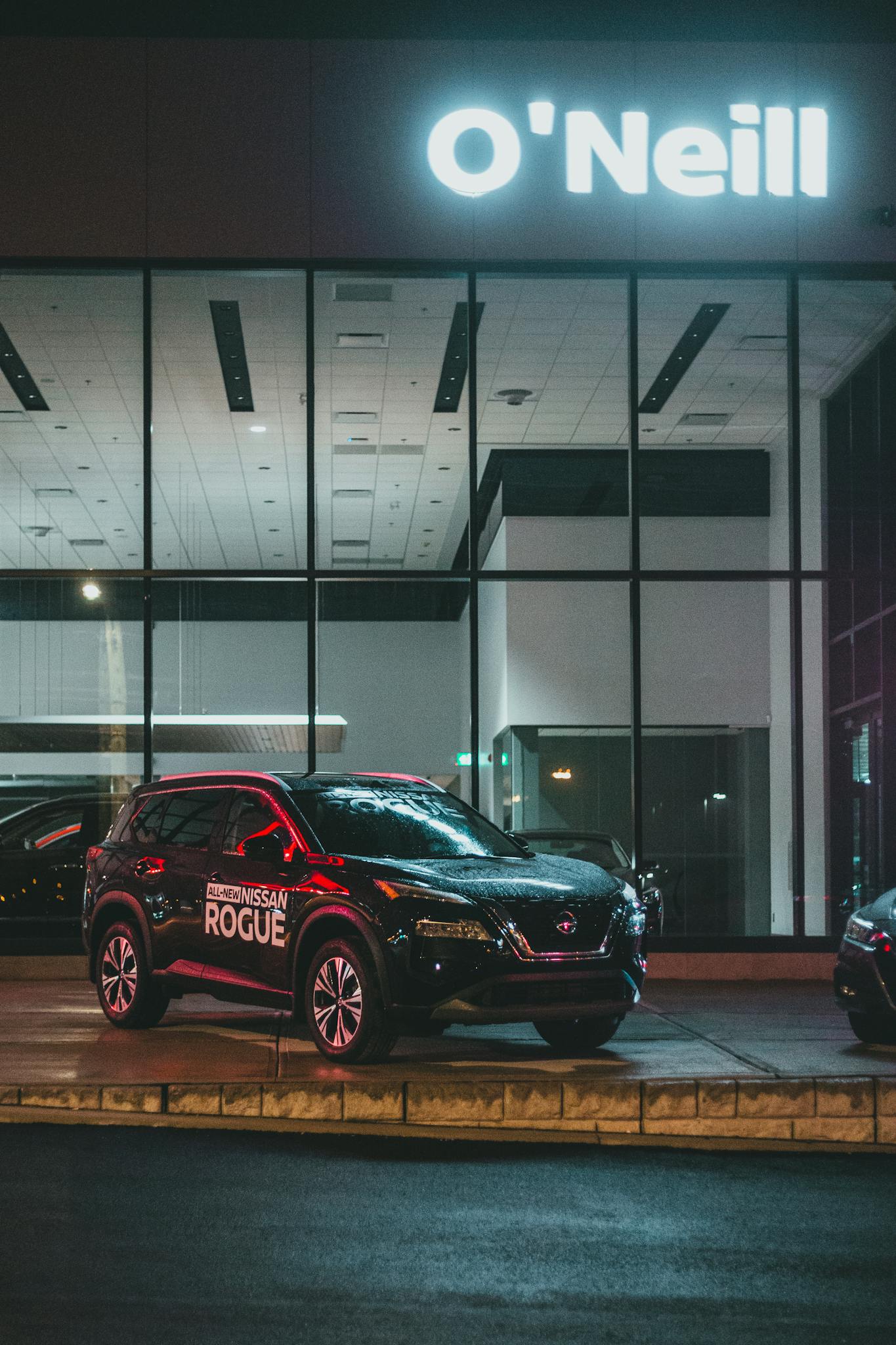 A Nissan Rogue displayed outside an illuminated dealership at night.