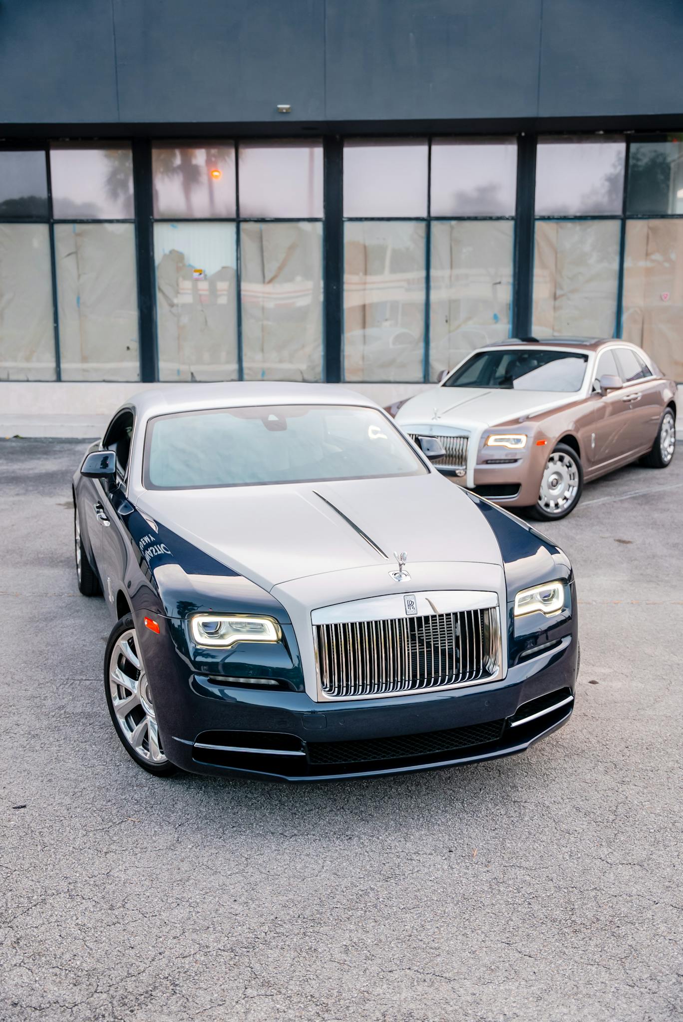 Two Rolls-Royce Wraith vehicles in front of a modern building, showcasing luxury design.
